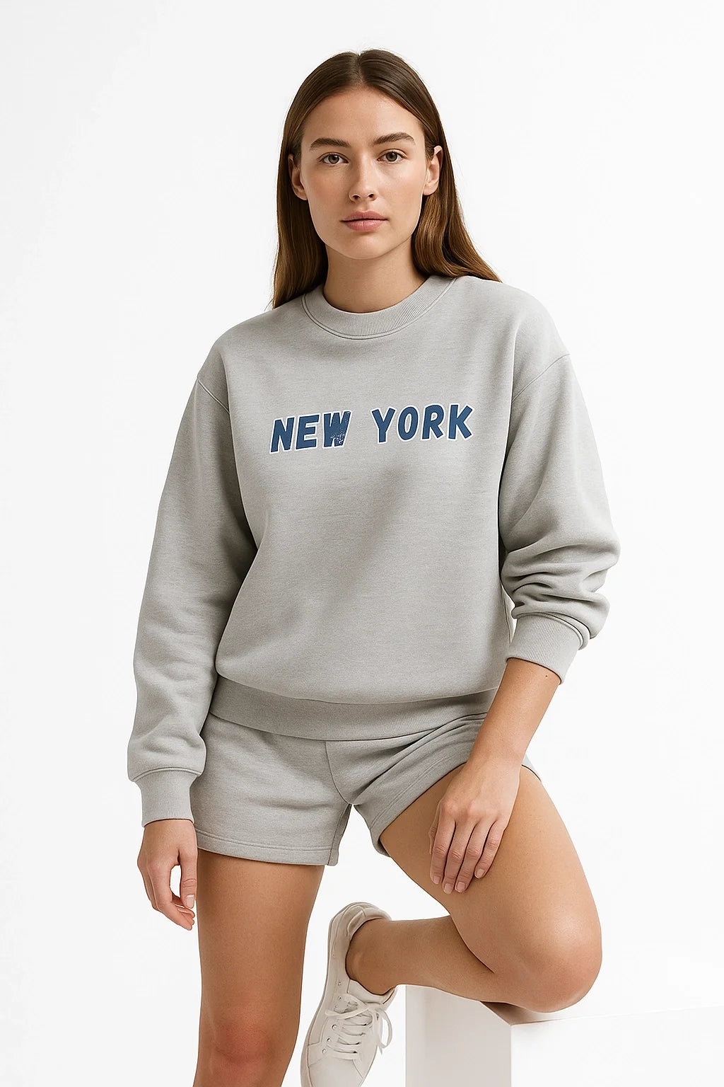 Woman wearing a gray sweatshirt with 'New York' text and matching shorts on a white background