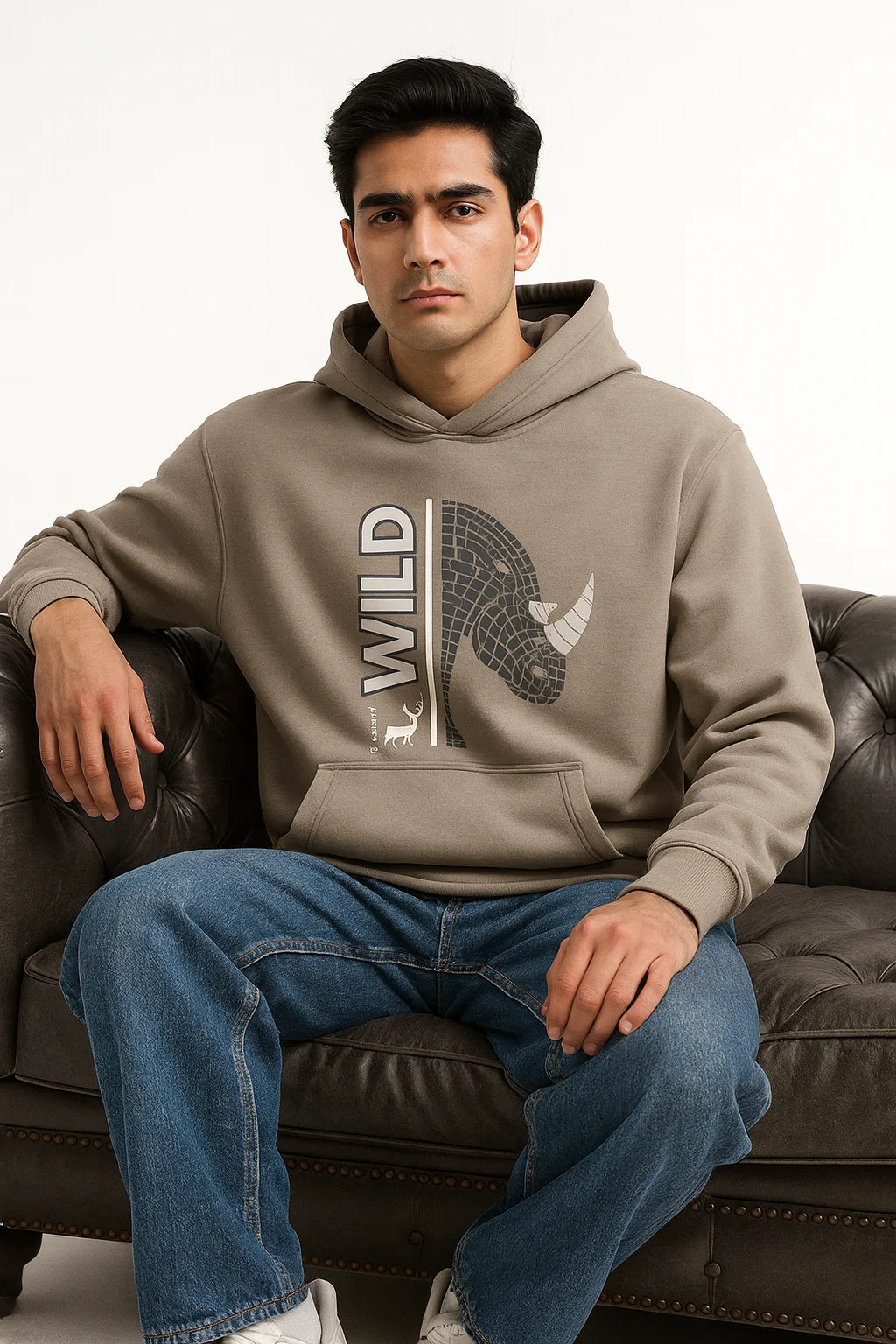 Man wearing a Grey hoodie with a graphic design sitting on a brown leather couch.