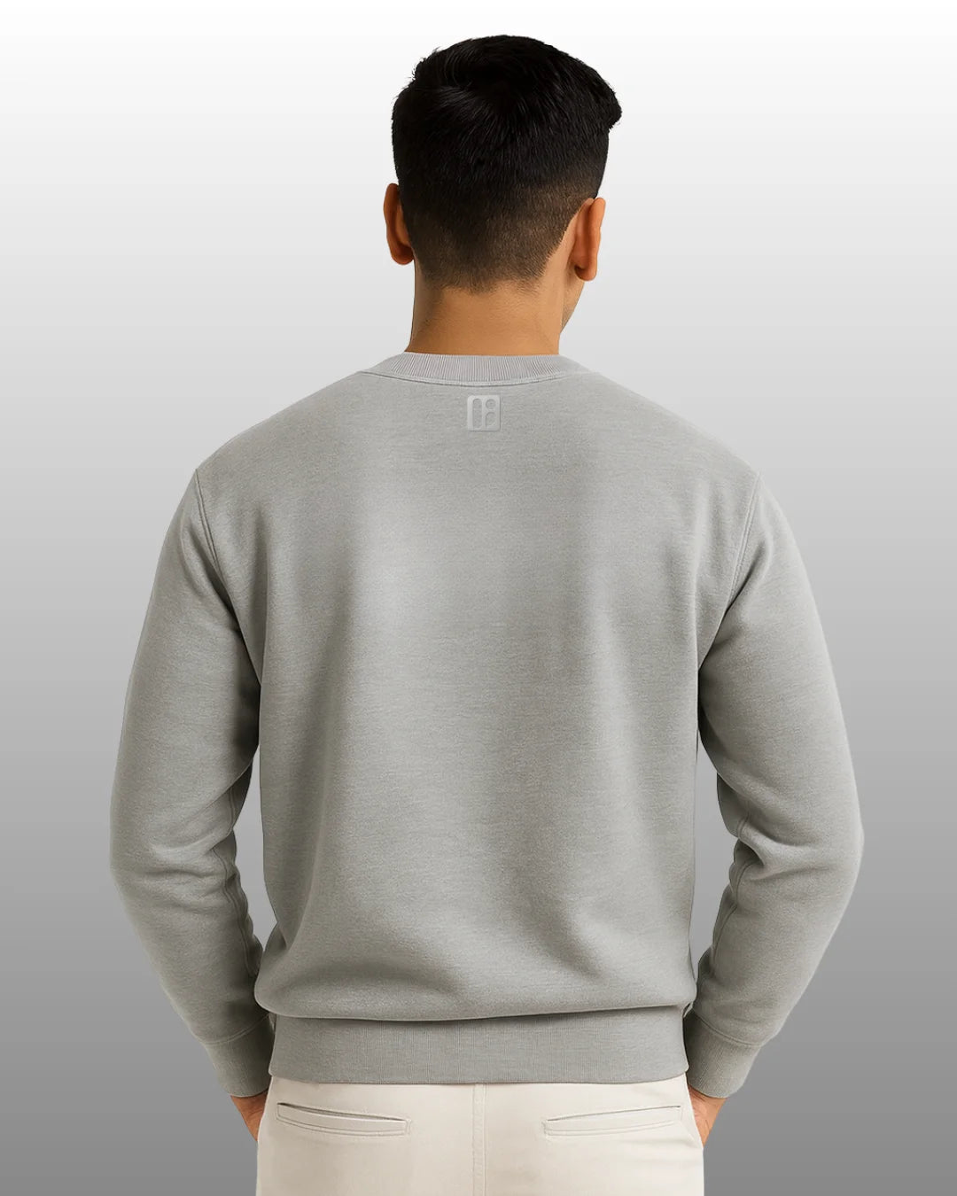 Person wearing a gray sweatshirt with a logo on the back against a plain background