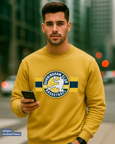 Man wearing a yellow sweatshirt with a logo, holding a phone, on a blurred city street background.