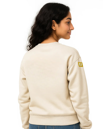 Person wearing a beige sweatshirt with a logo on the sleeve against a white background