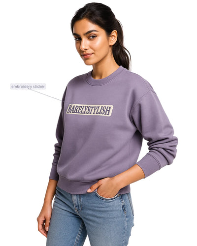 Woman wearing a purple sweatshirt with 'BARELYSTYLISH' text, standing against a white background.