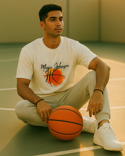 Man sitting on a basketball court with a basketball, wearing a white t-shirt with a graphic design.