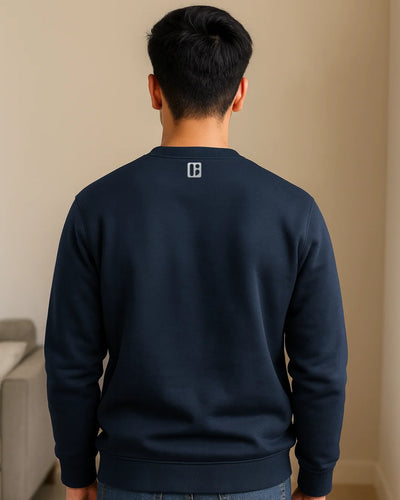 Person wearing a navy blue sweatshirt with a logo on the back, standing against a beige wall.