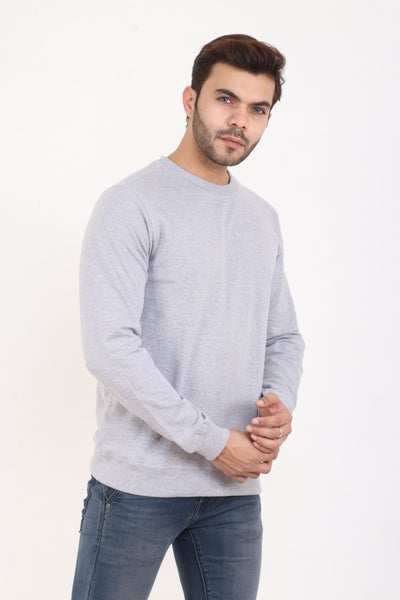 A man wearing a light grey solid sweatshirt and blue jeans.
