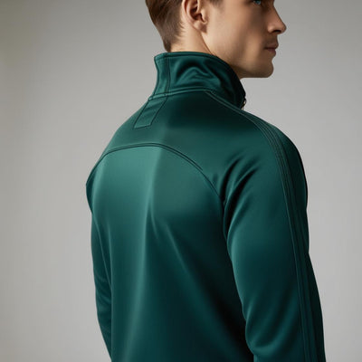A man wearing a dark green, lightweight, athletic fabric BarelyStylish tracksuit with a zippered jacket and pants. 